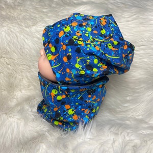 May include: Blue beanie and neck warmer set with a paint splatter pattern in black, orange, green, and yellow.