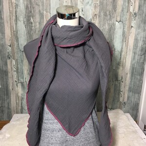 May include: Gray cotton scarf with a pink trim. The scarf is folded and displayed on a mannequin.