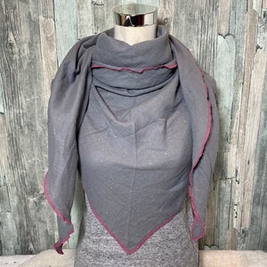 May include: A gray triangular scarf with a pink trim. The scarf is made of a soft, textured fabric and has a subtle shimmer.