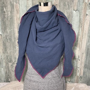 May include: A blue cotton scarf with a pink zig-zag trim. The scarf is folded and displayed on a mannequin.