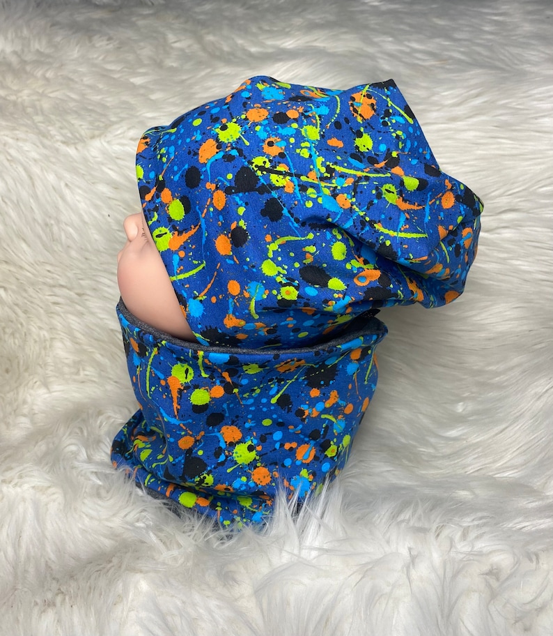 May include: A blue and black beanie with a colorful paint splatter pattern. The beanie is made of soft, comfortable fabric and is perfect for keeping warm in the winter.