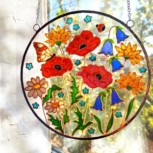 May include: A round stained glass panel featuring a vibrant floral design. The artwork includes red poppies, bluebell flowers, and orange daisies, with a butterfly and ladybug. The panel is framed with a black border and hangs from a chain.