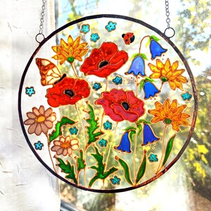 May include: A round stained glass panel featuring a vibrant floral design. Red poppies, yellow daisies, and blue bellflowers are depicted, along with a butterfly and ladybug. The artwork is framed with a black border and hangs from a chain.