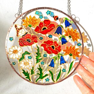 May include: A round, stained glass window featuring a colorful floral design. Red poppies, orange and yellow flowers, bluebells, and white daisies are depicted with green leaves. A butterfly and ladybug are also included.