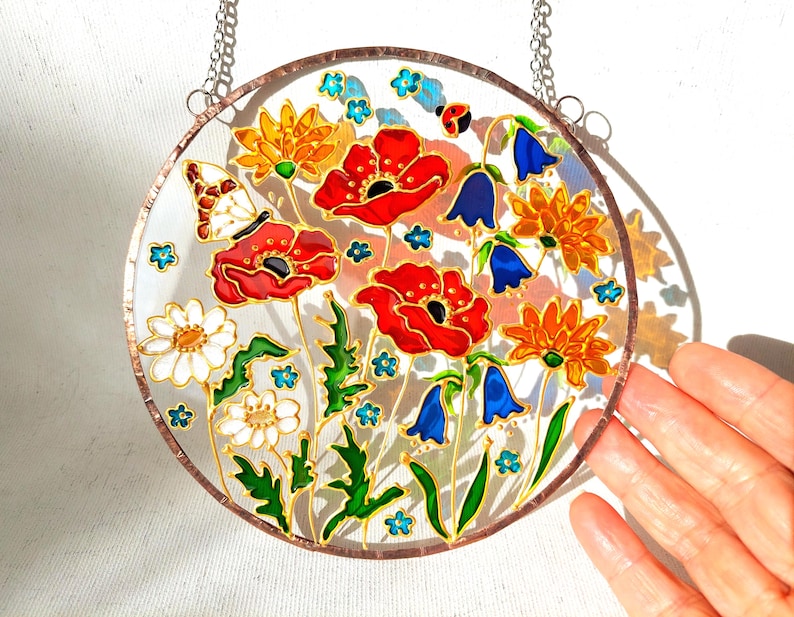 May include: A round, stained glass window featuring a colorful floral design. Red poppies, orange and yellow flowers, bluebells, and white daisies are depicted with green leaves. A butterfly and ladybug are also included.