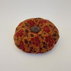 May include: A small, round, brown and red pincushion with a floral pattern and a wooden button in the centre.