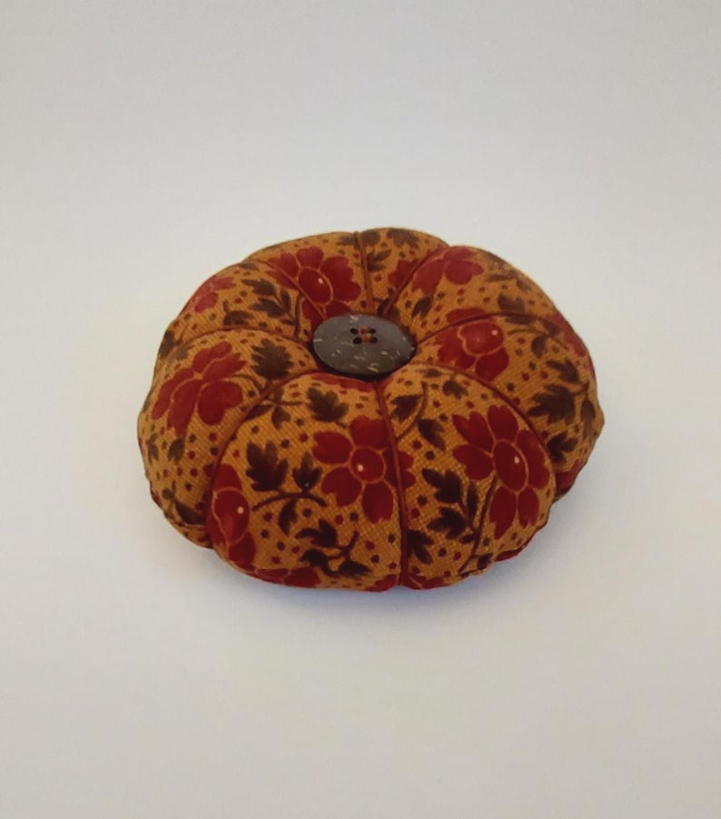 May include: A small, round, brown and red pincushion with a floral pattern and a wooden button in the centre.