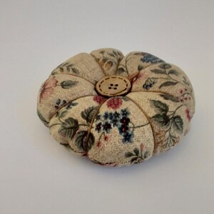 May include: A small, round, floral patterned pincushion with a wooden button in the centre.