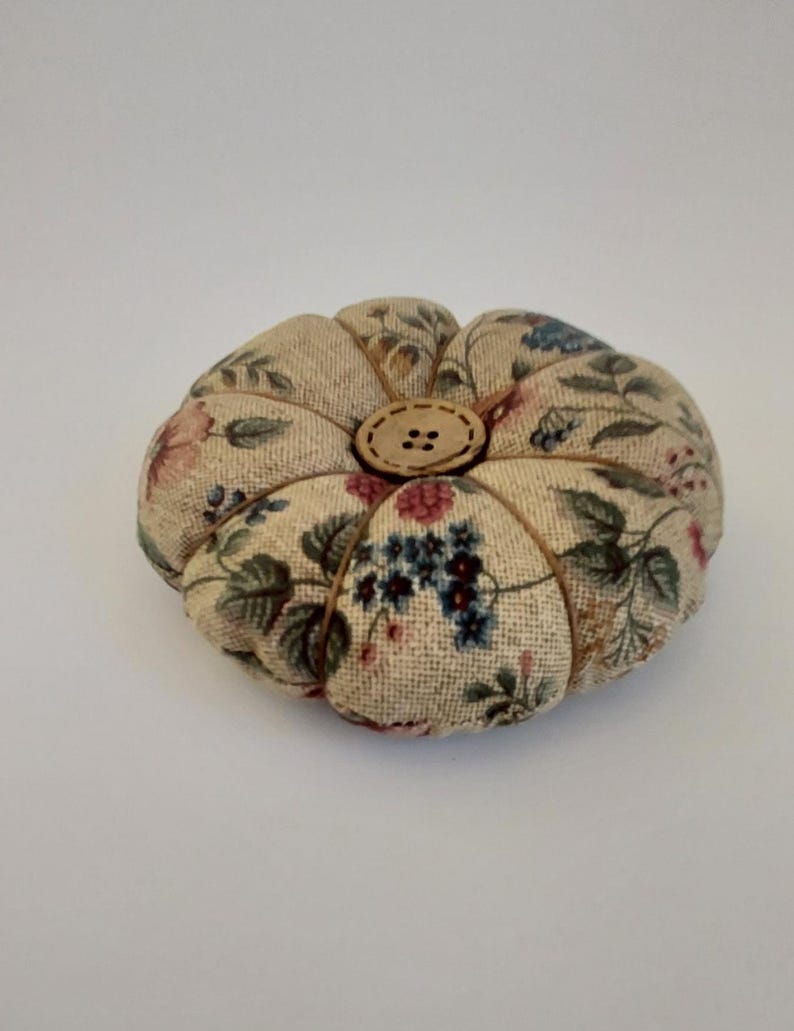 May include: A small, round, floral patterned pincushion with a wooden button in the centre.