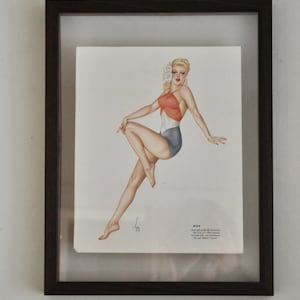 May include: Framed vintage pin-up illustration of a woman in a red, white and blue swimsuit. The woman is sitting with her leg crossed and a flower behind her ear. The illustration is titled "June" and includes a quote about the month.