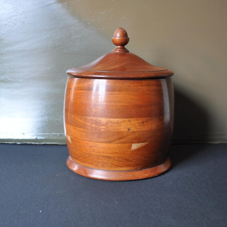 May include: A wooden container with a lid and a rounded shape. The container is made of light brown wood with a smooth finish. The lid has a small knob on top.