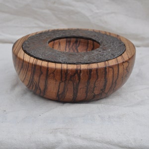 May include: A wooden bowl with a dark brown and black wood grain pattern. The bowl has a round, gray stone inlay in the center.