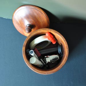 May include: A wooden container with a lid, open to reveal various items inside, including a roll of tape, a red screwdriver, a black marker, a white marker, a white tube, and a black and silver object.