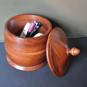 May include: A wooden box with a lid, the box is open and has a few items inside, including a pink lipstick, a black eyeliner, and a white tube of lip balm.