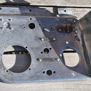 May include: A silver metal panel with two circular cutouts and several smaller holes. The panel has a worn, aged appearance with some rust spots.
