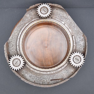 May include: A circular metal tray with a wooden center and three metal gears around the edge. The tray is made from recycled aircraft parts.