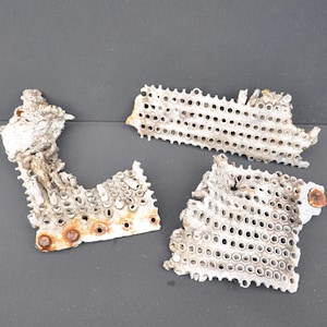 May include: Three pieces of a white metal grate with a pattern of small holes. The metal is rusted in places.