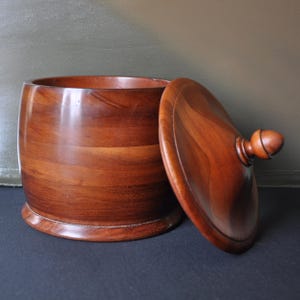 May include: A wooden bowl with a lid. The bowl is made of dark wood with a natural grain pattern. The lid has a knob on top.
