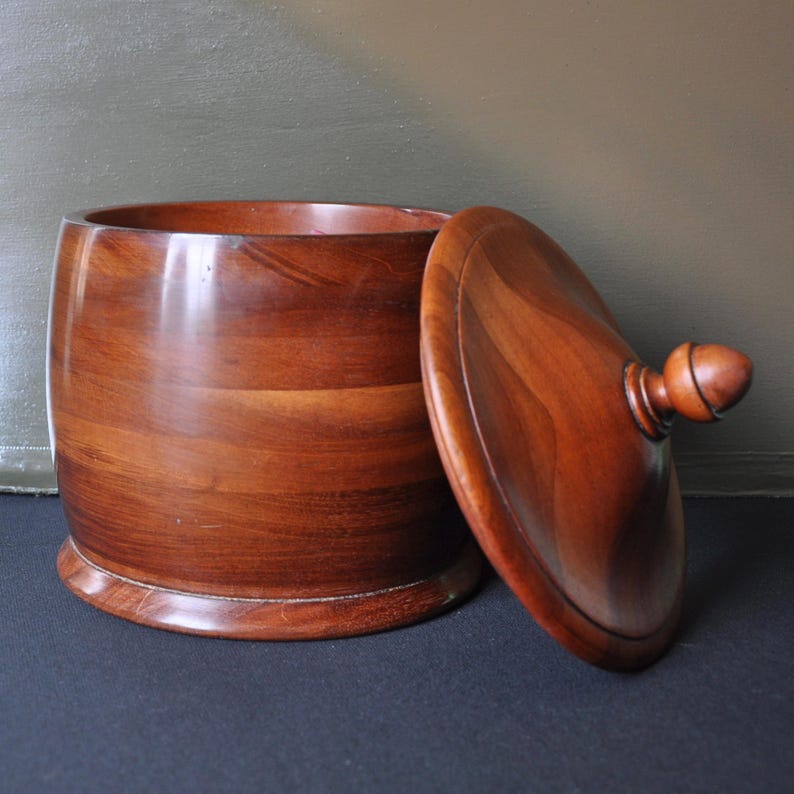 May include: A wooden bowl with a lid. The bowl is made of dark wood with a natural grain pattern. The lid has a knob on top.