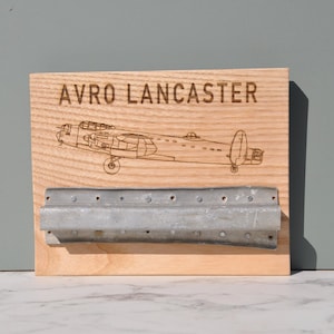 May include: A wooden sign with a laser-engraved image of an Avro Lancaster bomber plane. The sign has a metal bracket attached to the bottom.