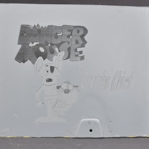 May include: A black and white illustration of Danger Mouse and his sidekick, a hamster named Penfold. The image is on a gray background with the text "Danger Mouse" and "Penfold's Chief" in a stylized font.