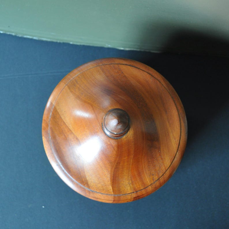 May include: A wooden lidded box with a rounded top and a small knob on the top. The box is made of dark wood with a smooth finish.