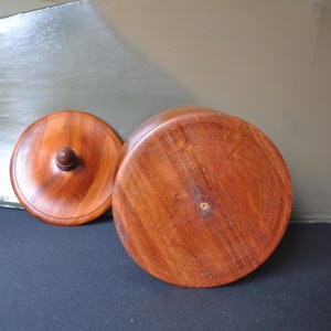 May include: A wooden bowl with a lid. The bowl is made of a dark reddish-brown wood and has a smooth, polished finish. The lid has a small knob on top.