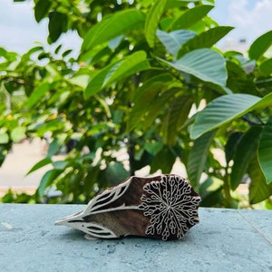 May include: A wooden printing block featuring a carved design of a flower with intricate details. The block is brown and has a natural wood finish.