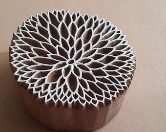 Puede incluir: Un sello de impresión de madera redonda con un diseño floral detallado tallado en la superficie. El diseño presenta un círculo central rodeado de pétalos intrincados.