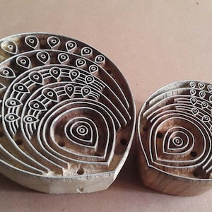 Puede incluir: Dos bloques de impresión de madera con intrincados diseños de plumas de pavo real. El bloque más grande es de forma semicircular, mientras que el bloque más pequeño es un círculo completo.