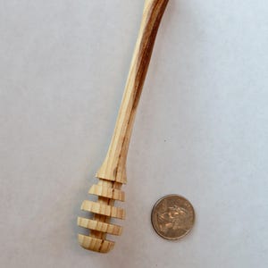 Pu&ograve; includere: Un mestolo per miele in legno con una finitura in legno naturale. Il mestolo ha un manico lungo e un'estremit&agrave; arrotondata e scanalata per raccogliere il miele. Il mestolo &egrave; circa delle dimensioni di una moneta da un euro.