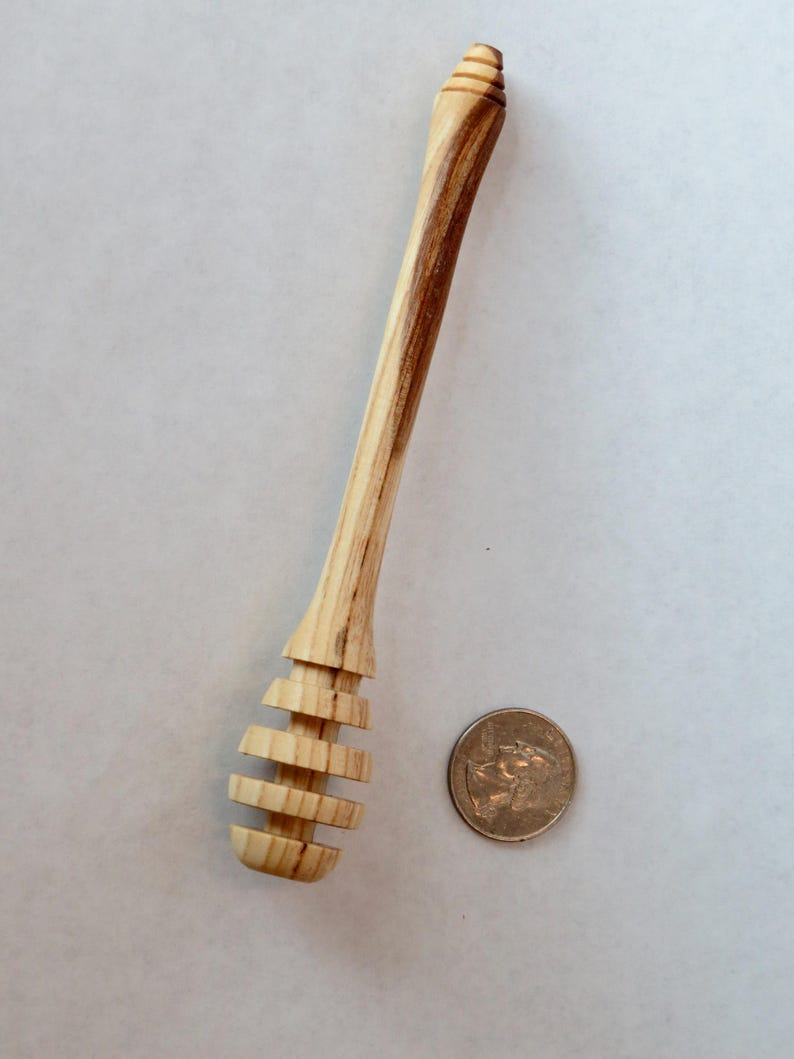Pu&ograve; includere: Un mestolo per miele in legno con una finitura in legno naturale. Il mestolo ha un manico lungo e un'estremit&agrave; arrotondata e scanalata per raccogliere il miele. Il mestolo &egrave; circa delle dimensioni di una moneta da un euro.