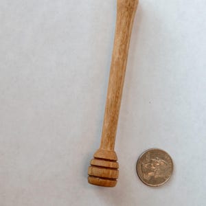 Pu&ograve; includere: Un mestolo di legno per il miele con un'estremit&agrave; arrotondata e scanalata e un manico lungo e sottile. Il mestolo &egrave; circa delle dimensioni di una moneta da 20 centesimi di euro.