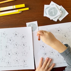 May include: A child's hand places a number sticker on a star-shaped worksheet. The worksheet has stars with numbers inside and the text "He counts the stars and knows them all by name. Psalm 147:4".