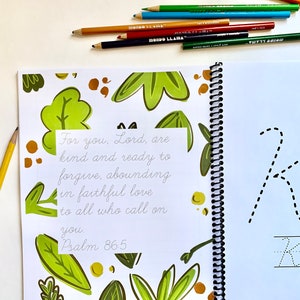 May include: A spiral bound notebook with a green and brown floral design. The notebook has a white page with a handwritten bible verse: "For you, Lord, are kind and ready to forgive, abounding in faithful love to all who call on you. Psalm 86:5". The opposite page has a dotted line drawing of the letter "K" and the word "Kind" written below.