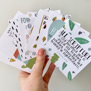 May include: A set of colorful cards with inspirational quotes and scripture verses. The cards feature a variety of patterns and designs, including swirls, leaves, and geometric shapes. The text on the cards is in black and white. The cards are perfect for encouraging and uplifting others.