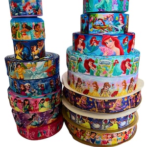 Può includere: Una collezione di rotoli di nastro impilati con vari disegni di principesse Disney. I nastri mostrano illustrazioni colorate di personaggi come Ariel, Belle e Cenerentola. I nastri sono in tonalità di blu, rosa, viola e giallo.