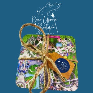 May include: A set of square coasters featuring a colourful theme park map, tied together with natural brown twine. A small, rectangular tan paper tag is attached to the twine, displaying a circular blue logo with the text Once Upon a Boutique.
