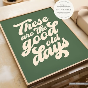 May include: A rectangular wall art print featuring a dark green background with the cream-coloured text "These are the good old days" in a bold, cursive script font. The print is displayed in a light wood frame, showcasing a digital design.
