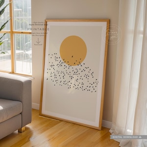 Puede incluir: Una impresión digital descargable con un diseño minimalista que presenta un gran círculo amarillo y una bandada de pájaros negros volando hacia arriba. La impresión tiene un fondo beige y está enmarcada en un marco de madera claro.