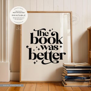 May include: A printable wall art design featuring the text "The book was better" in a retro font style with black stars. The design is on a white background and is framed in a light wood frame.
