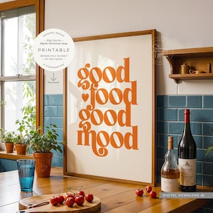Könnte beinhalten: Gerahmter Druck mit den Worten "good food good mood" in orangefarbenen Buchstaben. Der Druck wird in einer Küchenumgebung mit einer Holztheke, einem Glas Wasser und einer Weinflasche angezeigt.