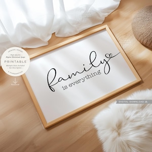 May include: A framed white print with the words "Family is everything" in black script. The print is in a light wood frame and sits on a wooden surface. A fluffy white rug and a woven basket are also visible.
