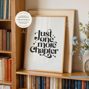 May include: A framed vertical print featuring the black text Just one more Chapter in a stylized font with small star accents. The print is displayed on a wooden shelf among various books, with a circular white label overlaying the top left.