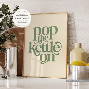 以下が含まれることがあります： クリーム色の背景に、緑色のスクリプトで「pop the kettle on」という言葉が書かれた額入りのプリント。 プリントは金のフレームに入っており、デジタルダウンロードです。 画像には、銀色のピッチャー、木のまな板、レモンのボウルが含まれています。