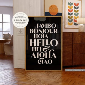 Puede incluir: Un estampado en blanco y negro enmarcado con la palabra "HELLO" en letras grandes y estilizadas, junto con saludos en varios idiomas. El estampado forma parte de una colección de arte mural, con otros estampados enmarcados visibles en el fondo.