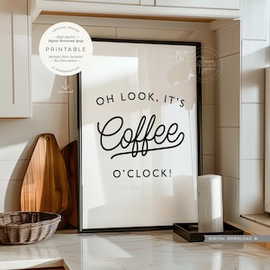 Peut inclure: Une impression d'art mural imprimable avec un design noir et blanc qui dit "Oh look, it's coffee o'clock!" L'impression est encadrée dans un cadre noir et est posée sur un comptoir.