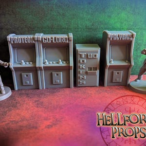 Op de afbeelding: Vier grijze arcadekasten met verschillende speltitels, waaronder "Proteo", "Go-Lord", "Polybius" en "Two Tokens". De kasten staan op een rood oppervlak met een zwart-wit symbool op de voorgrond.