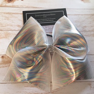 May include: A large white and iridescent silver cheer bow with a sparkly center. The bow is made of mesh fabric and has a swirl pattern.