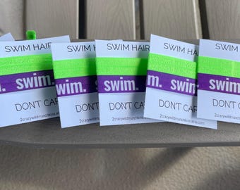 May include: Six elastic hair ties featuring a bright neon green and purple color scheme. Each tie is wrapped around a white card printed with the text SWIM HAIR DON'T CARE and 2crazywildmunchkins.etsy.com in black ink on the front.